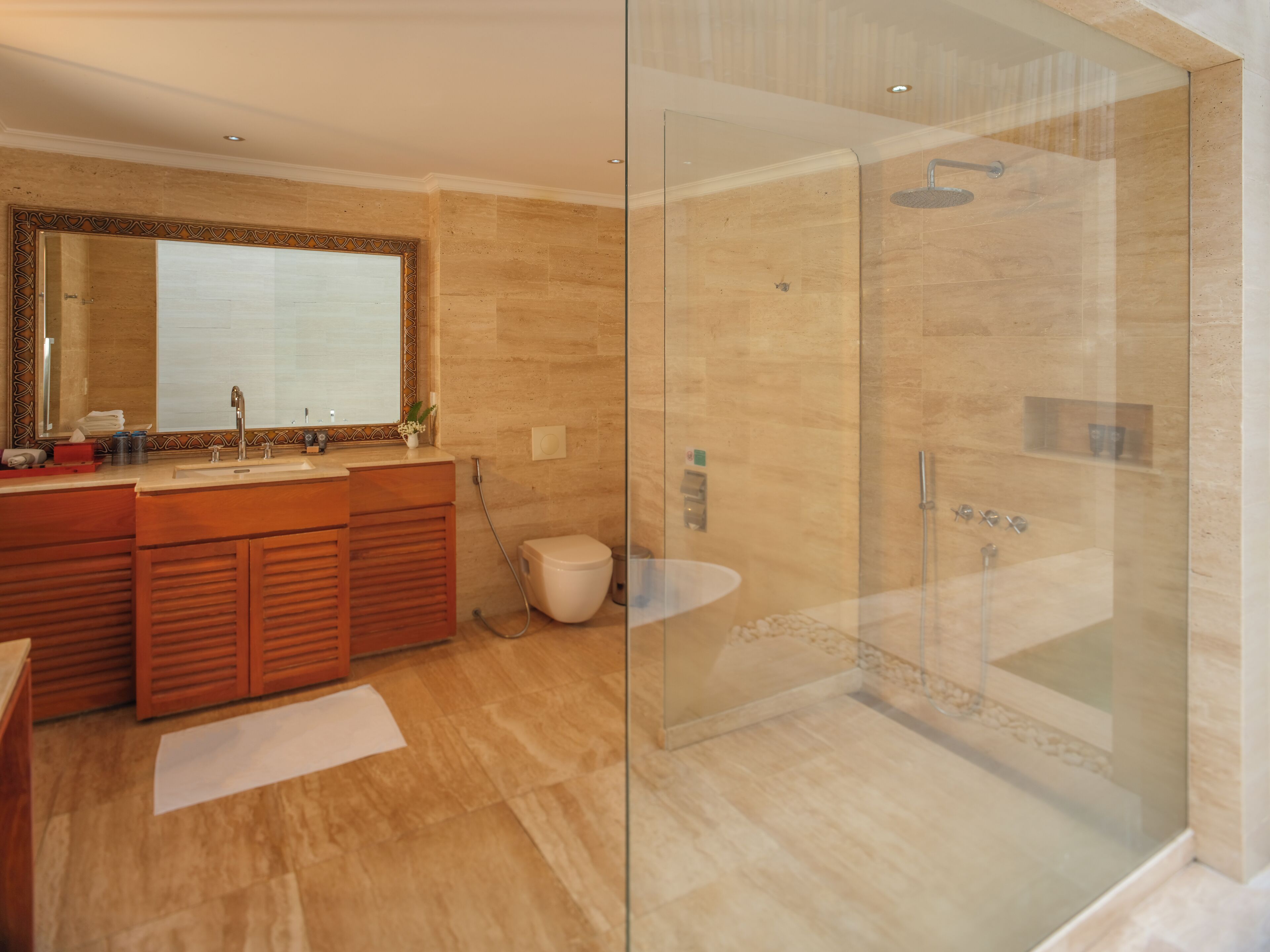 Un baño moderno con ducha envuelta en vidrio, tocador de madera y un espejo grande.