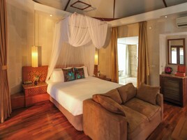 A spacious hotel room with a large bed, a sitting area with a sofa, a bedside table with a lamp, and a view of the outside through a glass door.