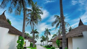 A pathway lined with palm trees and thatched-roof structures, leading to a beach. - Sunsea Resort (Mui Ne)