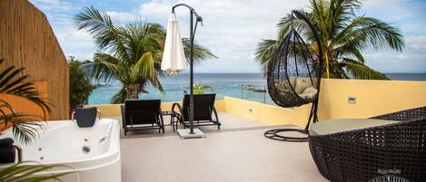 Un resort frente al mar con jacuzzi, sillas de descanso y vistas al océano.