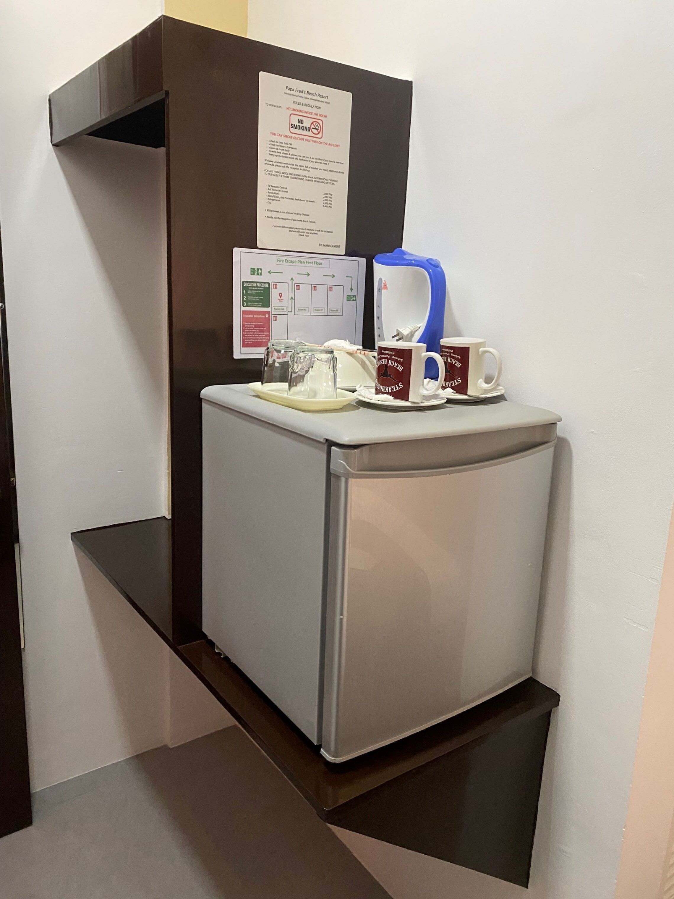 Une petite cuisine équipée d’un réfrigérateur, d’une machine à café et d’une tasse posée sur une petite table.