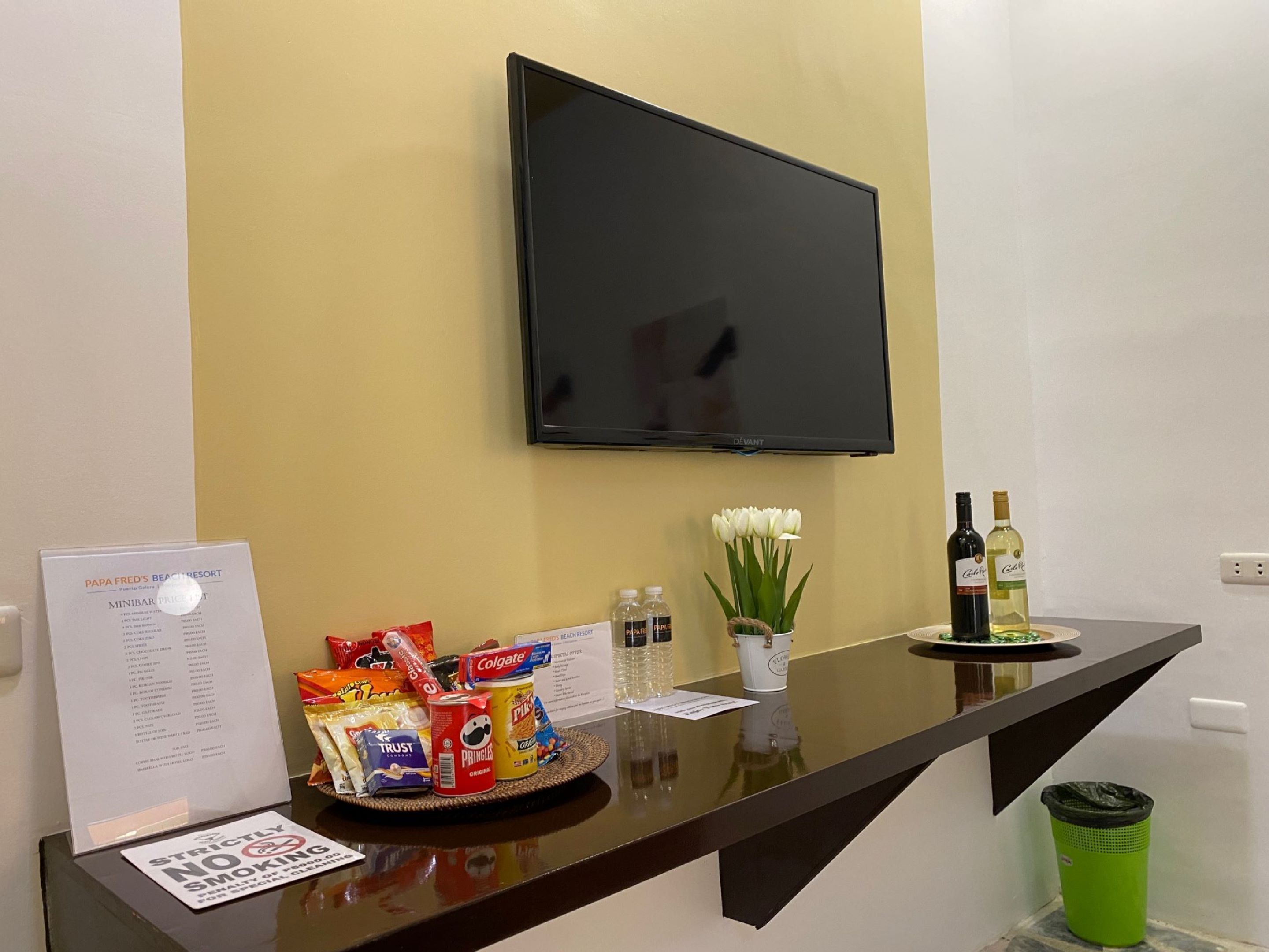 Un mostrador de recepción con un menú, aperitivos, una botella de vino y un jarrón de flores.