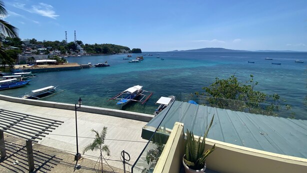 A coastal view with boats docked at a pier, a clear sky, and a distant mountain range.