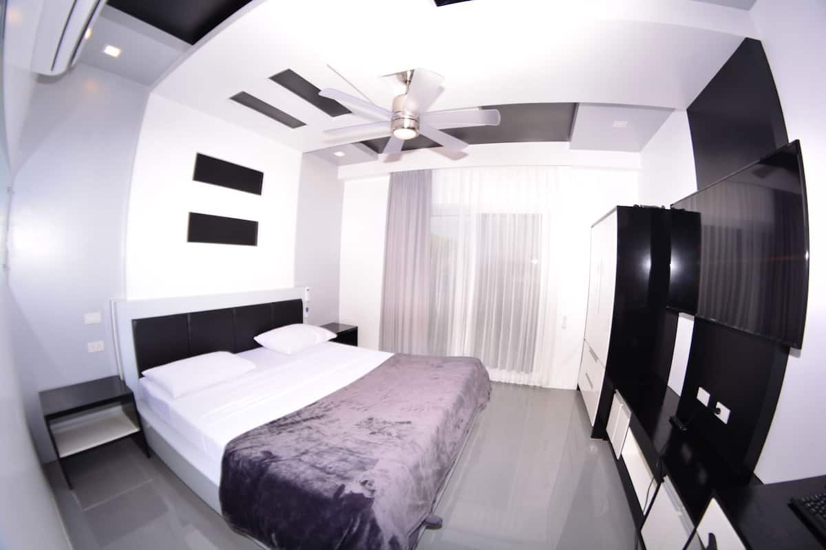 A modern hotel room with a bed, a desk, a TV, and a ceiling fan.