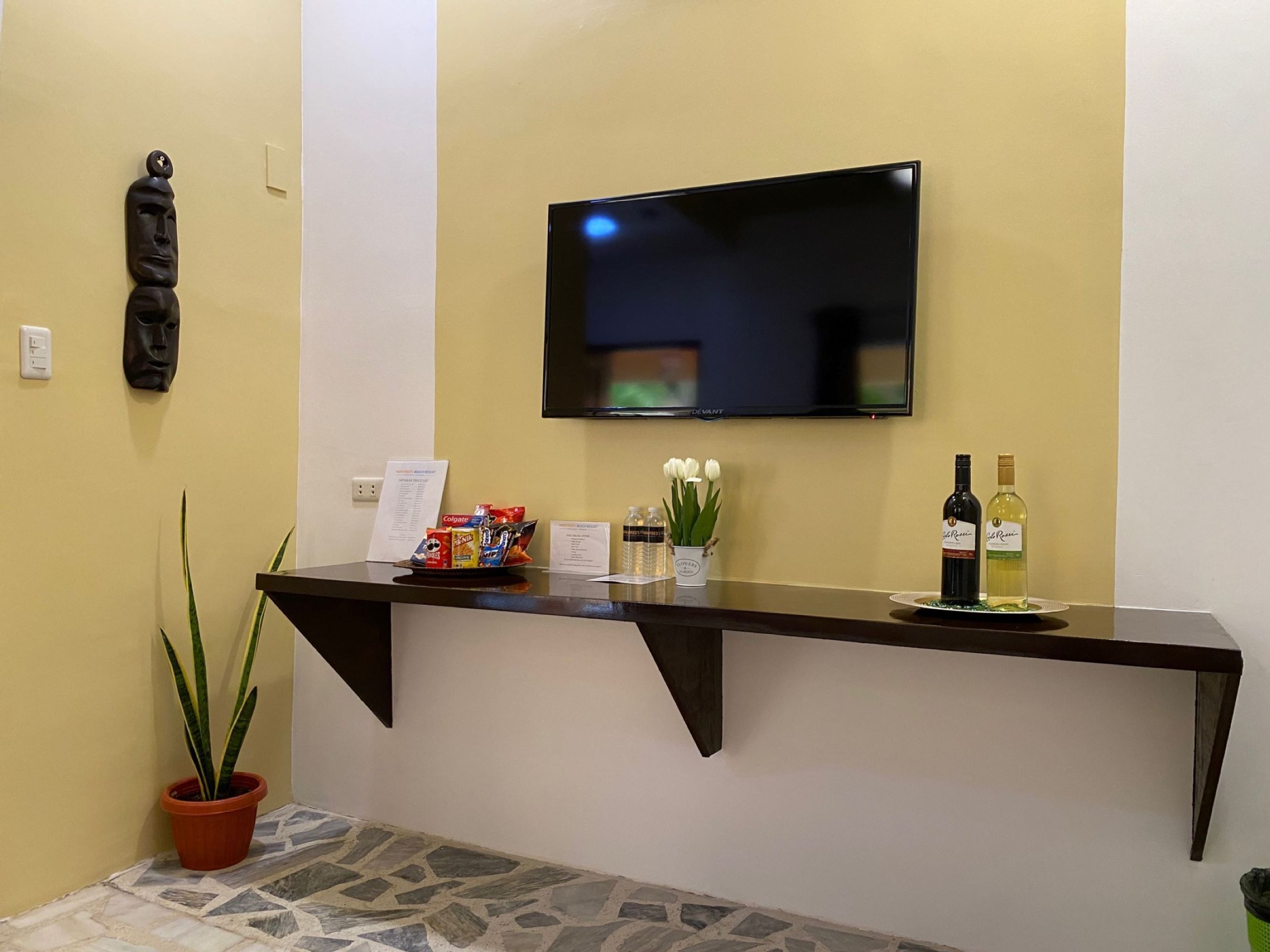 A reception area with a flat-screen TV mounted on the wall, a counter with snacks, a potted plant, and a wine bottle.