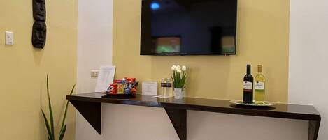A reception area with a flat-screen TV mounted on the wall, a counter with snacks, a potted plant, and a wine bottle.