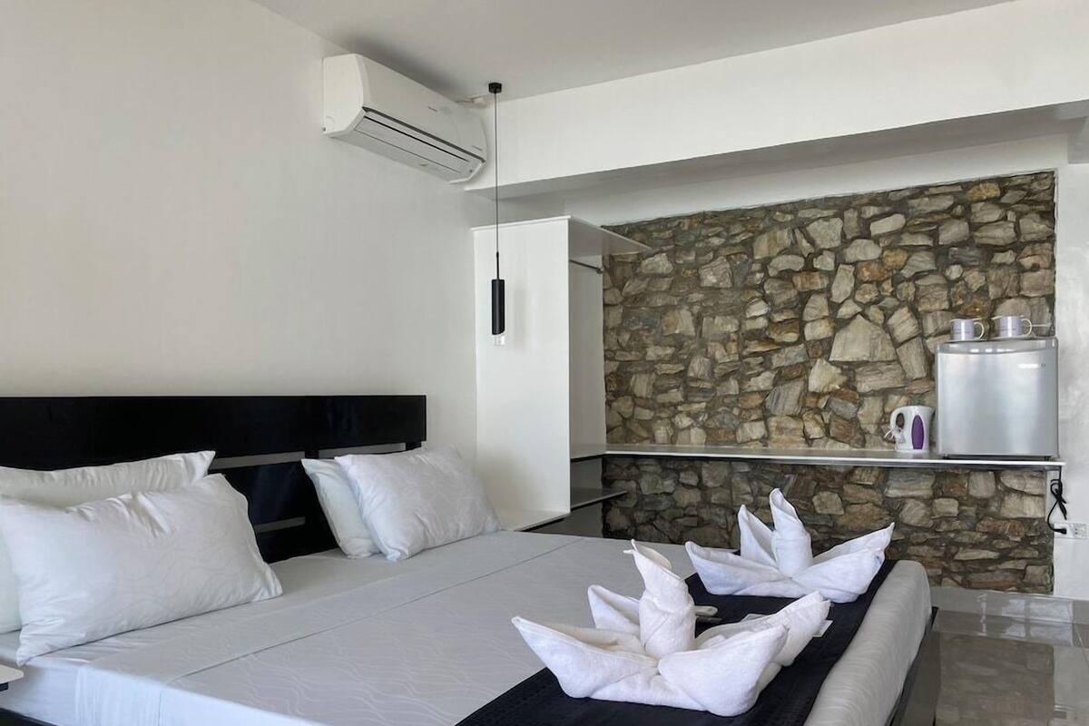 A hotel room with a bed, a stone wall, a coffee machine, and a shelf.