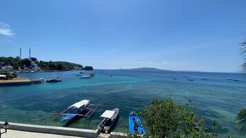 A coastal view with boats docked at a pier, clear blue water, and a distant mountain range.