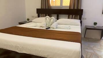 Cama bem arrumada com manta marrom, almofadas brancas e toalhas dispostas em formato de coração.
