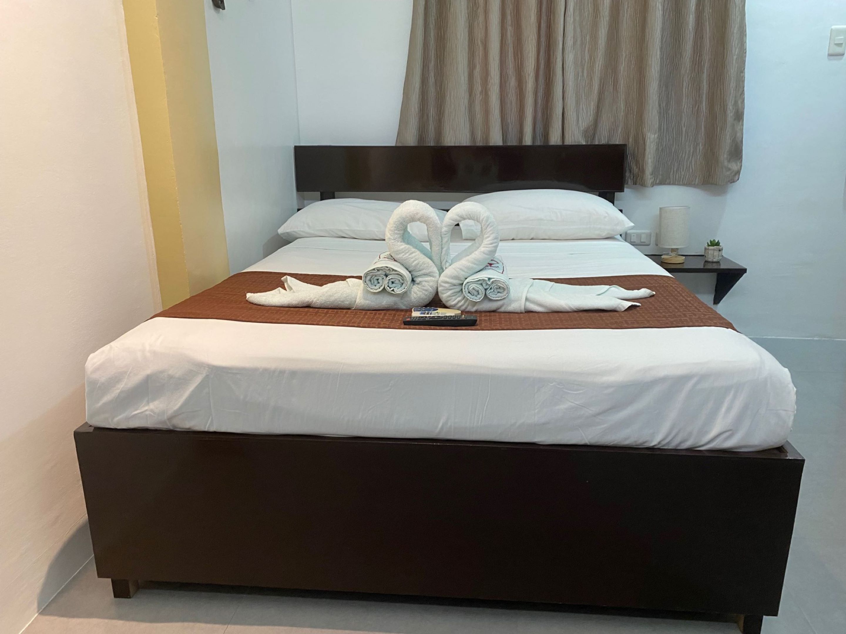 A hotel room with a bed, a nightstand, and a wall-mounted curtain.