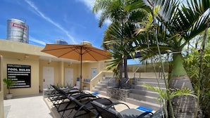 A poolside area with lounge chairs, a large umbrella, and a sign detailing pool rules.