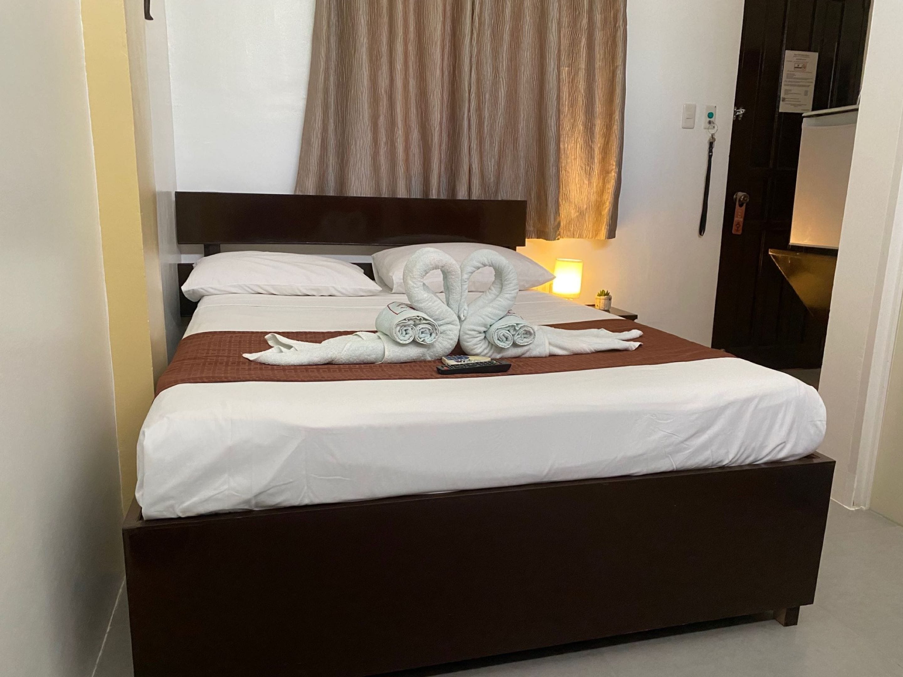 A hotel room with a bed, a brown headboard, a lamp, and a wall-mounted TV.