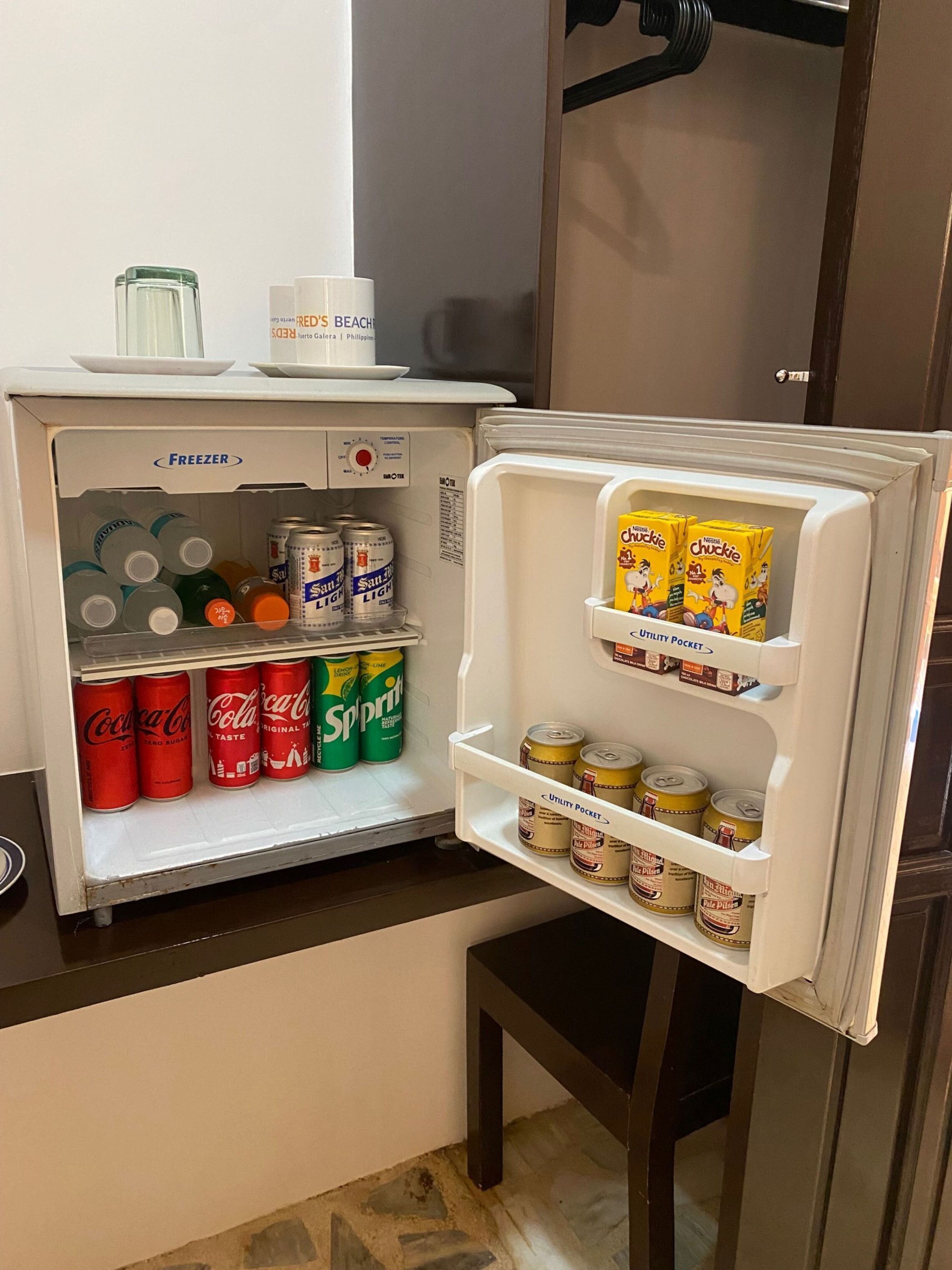 An open mini-fridge stocked with beverages and snacks.