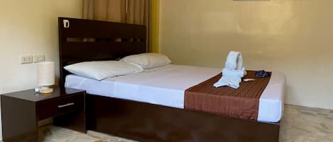 Una cama bien hecha con cabecera marrón, una mesita de noche con lámpara y una alfombra estampada en el suelo.