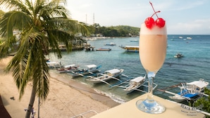 A beach view with boats, a palm tree, and a drink with cherries.