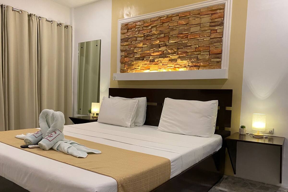 A hotel room with a bed, two bedside tables, a wall-mounted artwork, and a curtain.