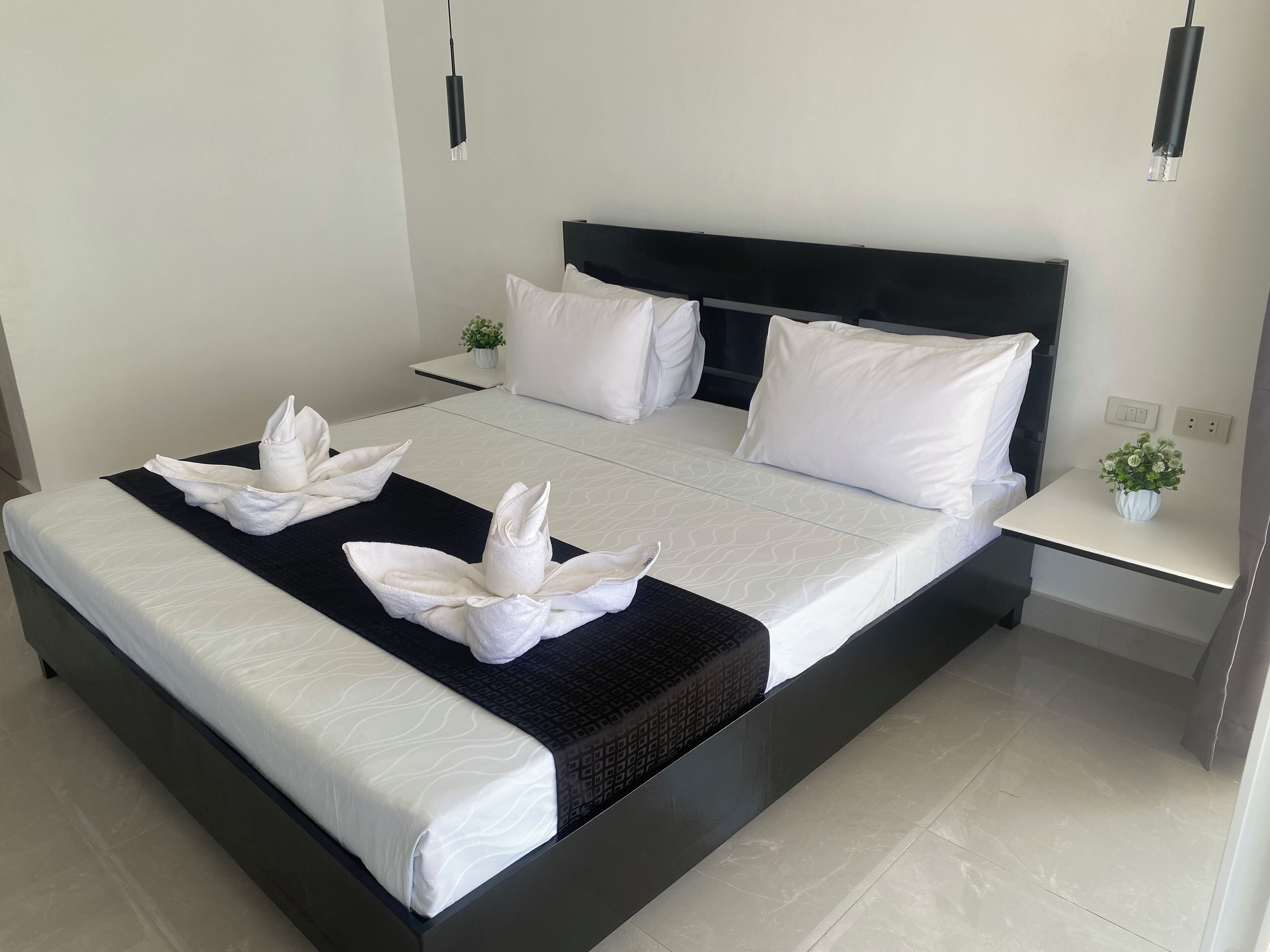 A modern hotel room with a large bed, white linens, a black headboard, and a small bedside table with a vase of flowers.
