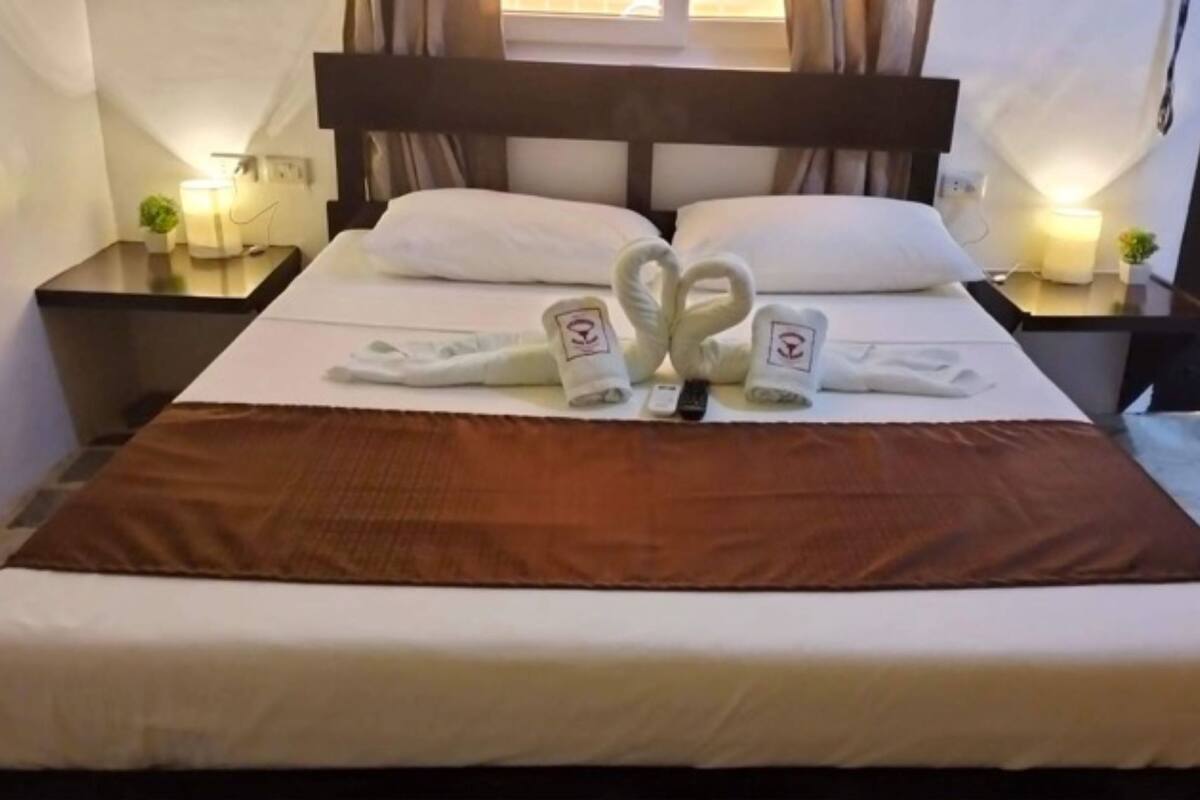 A neatly made bed with a brown blanket, white pillows, and two towels arranged in a heart shape on the bed.