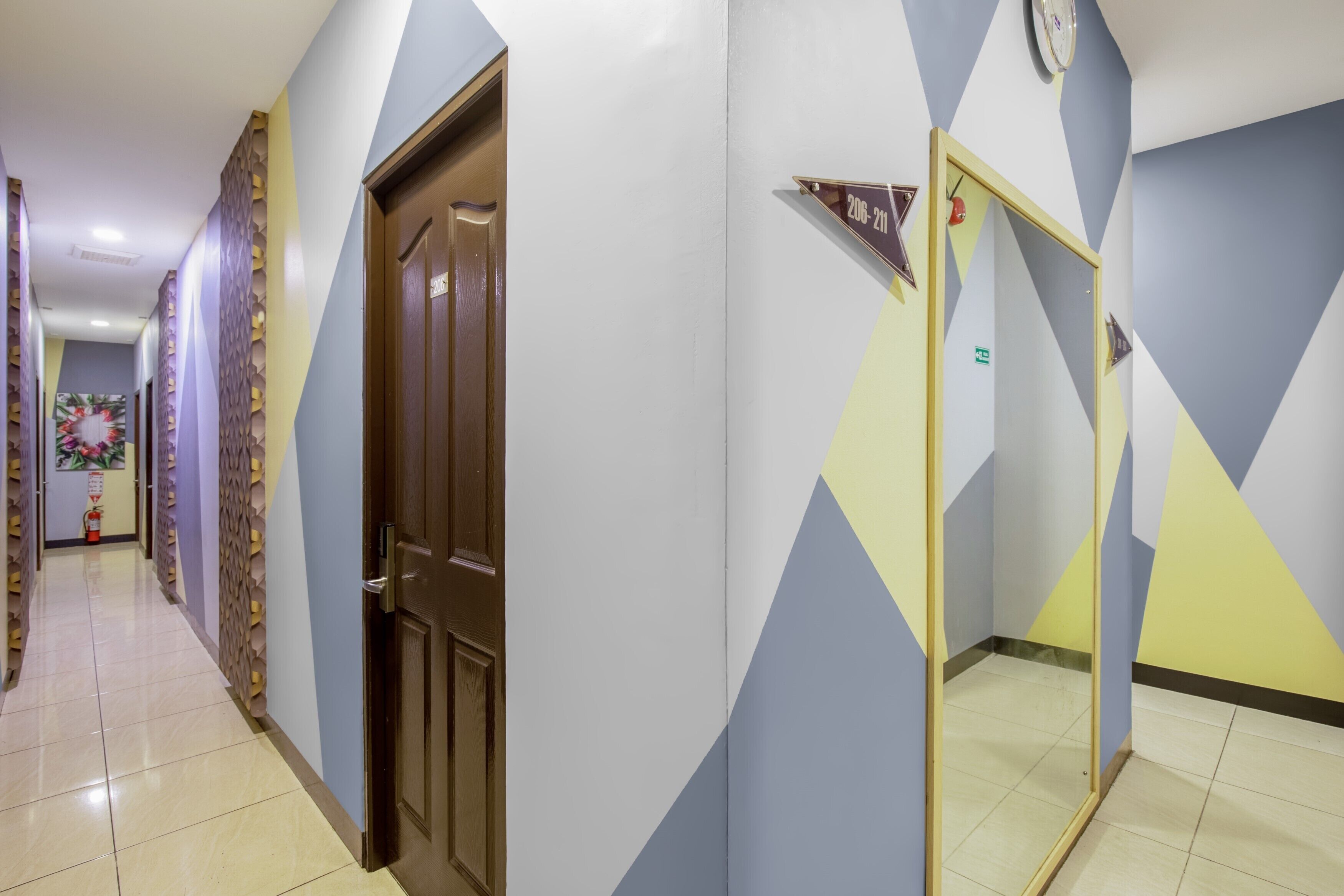 A hotel corridor with a wooden door, a mirror, and a wall with geometric patterns.
