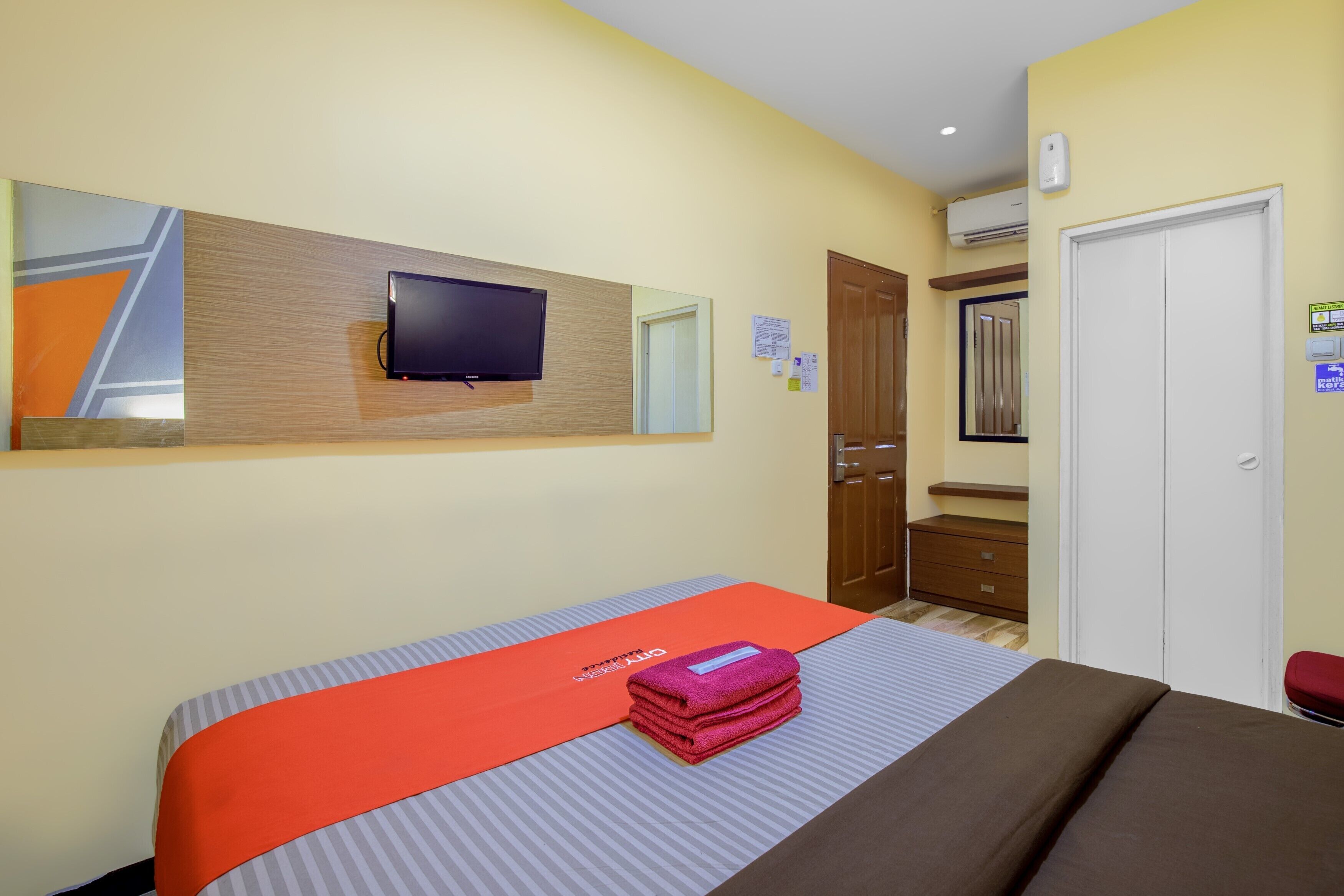 A hotel room with a bed, a television mounted on the wall, a wardrobe, and a door.