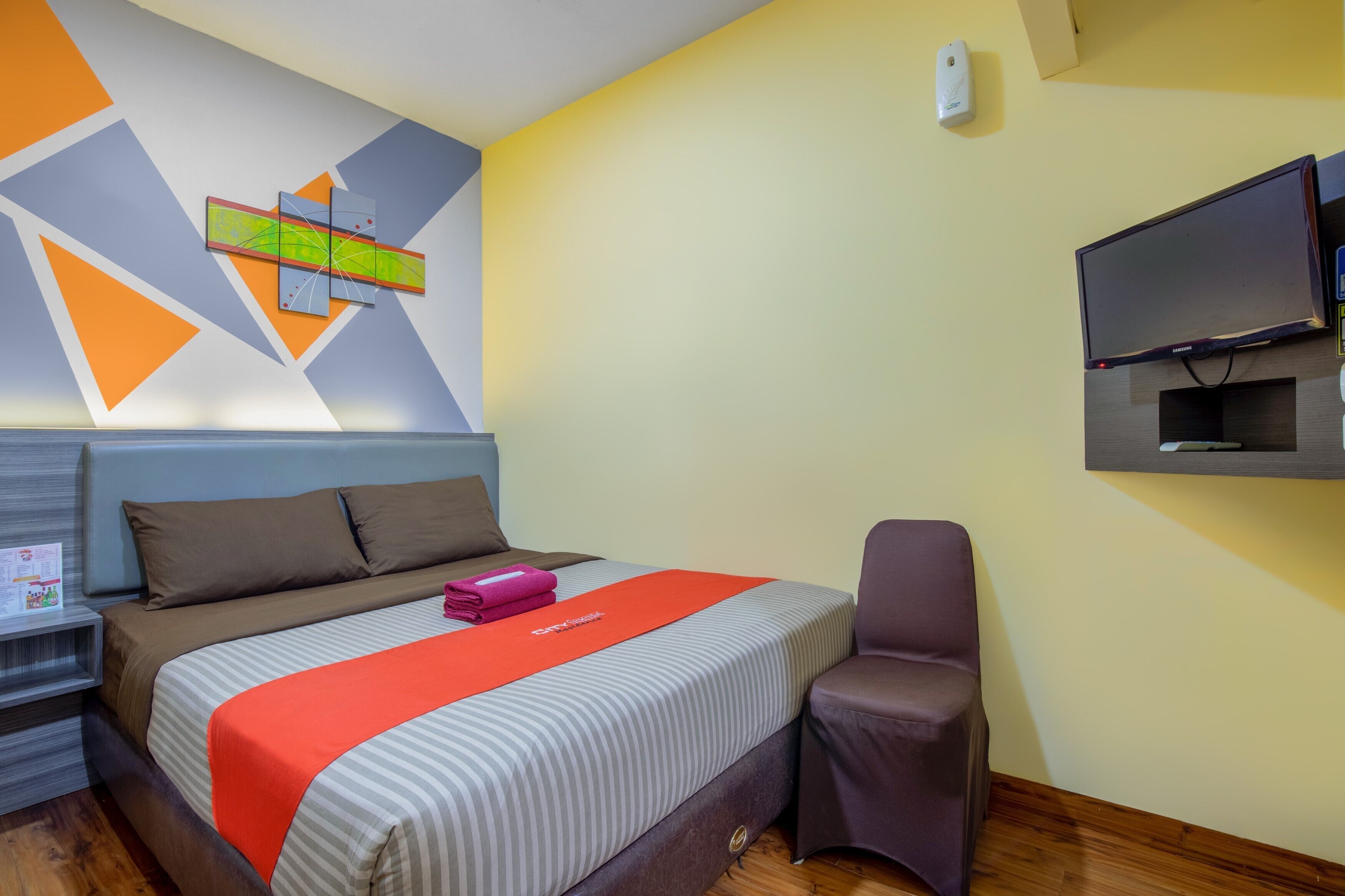 Een hotelkamer met een bed, een televisie, een stoel en een muur met geometrische patronen.