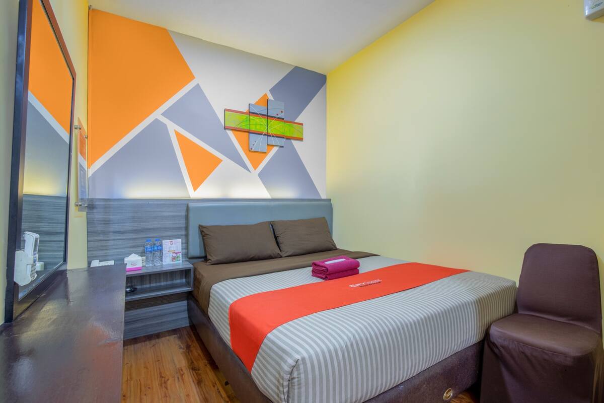 A hotel room with a bed, a chair, a nightstand, and a wall with geometric patterns.