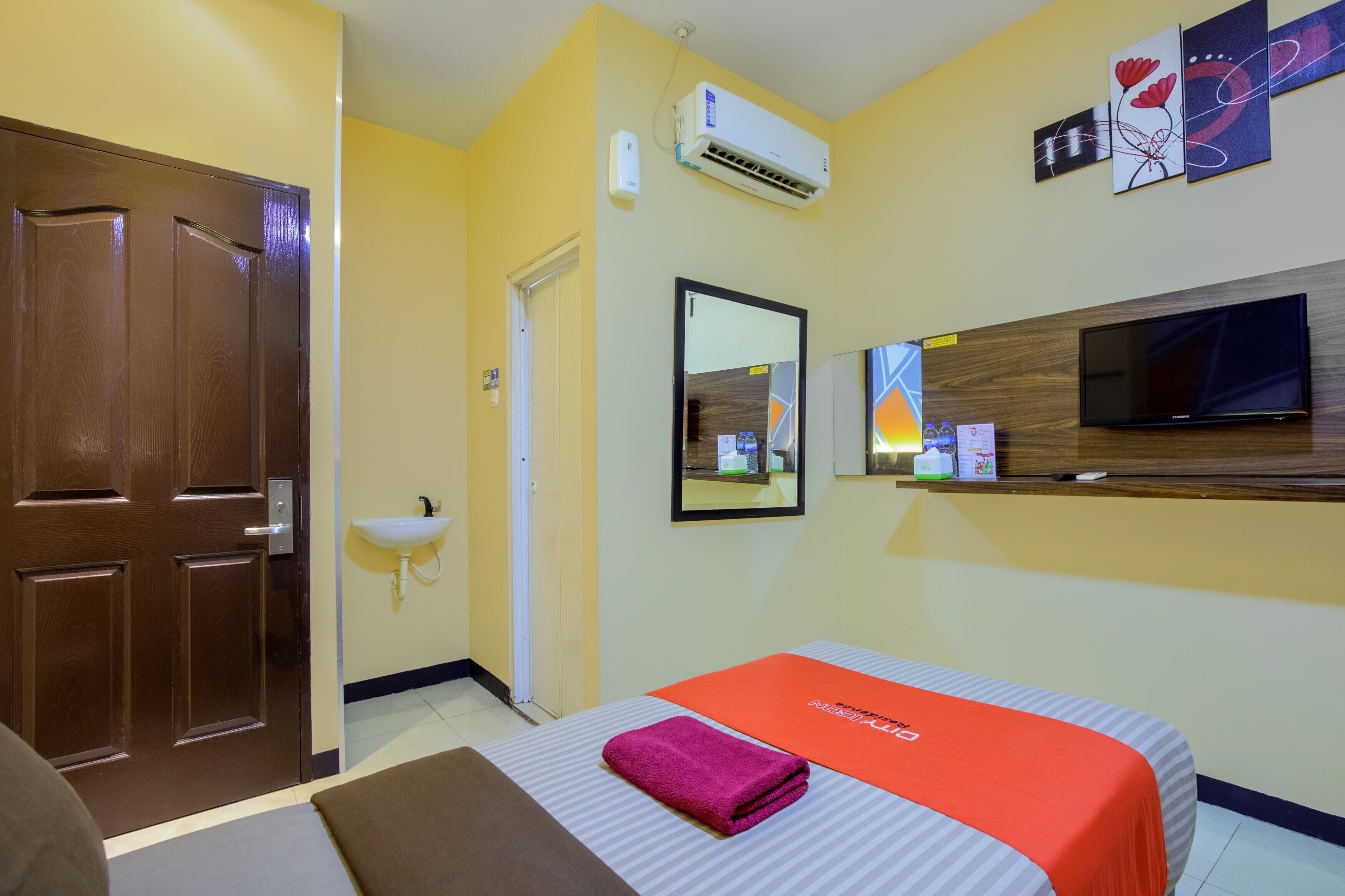 A hotel room with a bed, a TV, a mirror, an air conditioning unit, and a sink.