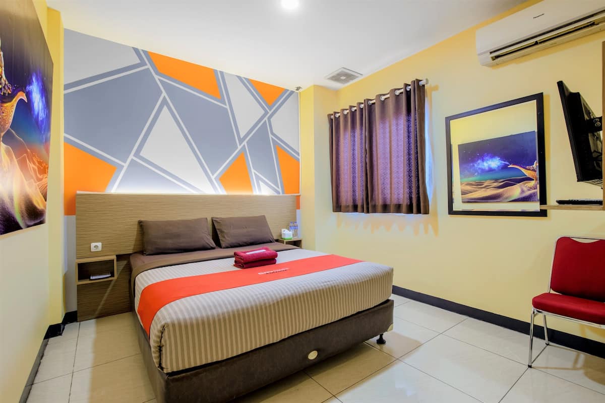 A hotel room with a bed, a nightstand, a red chair, a wall with geometric patterns, and a framed picture.