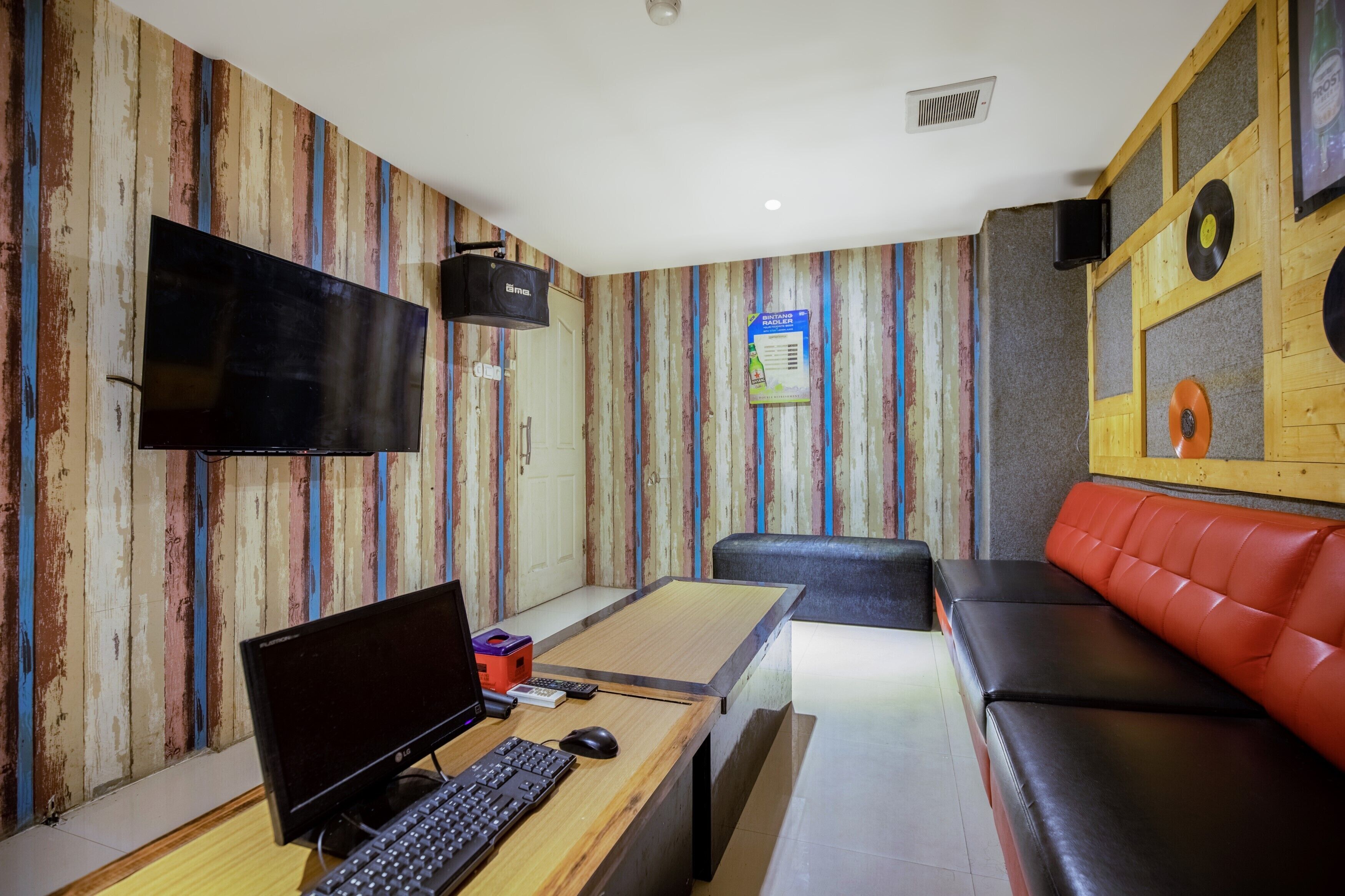Une pièce avec un mur en bois, un téléviseur à écran plat, un bureau avec un ordinateur, un canapé en cuir rouge et un haut-parleur fixé au mur.