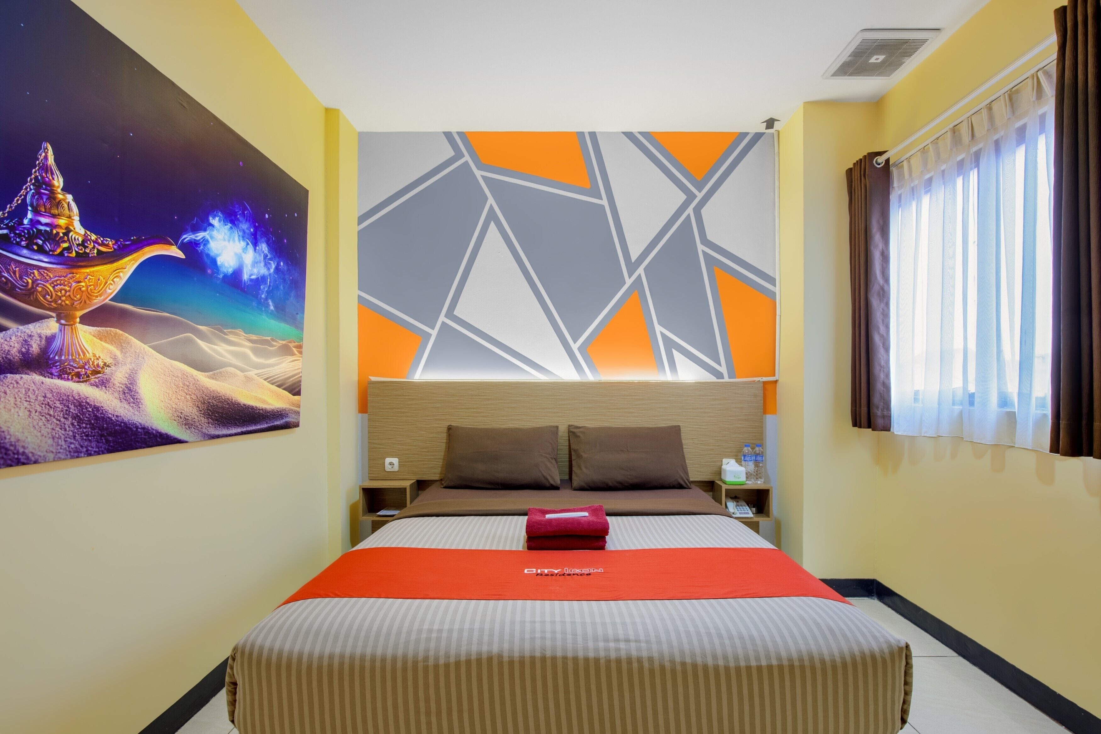 A hotel room with a large bed, a nightstand, a wall with a geometric pattern, and a window with curtains.