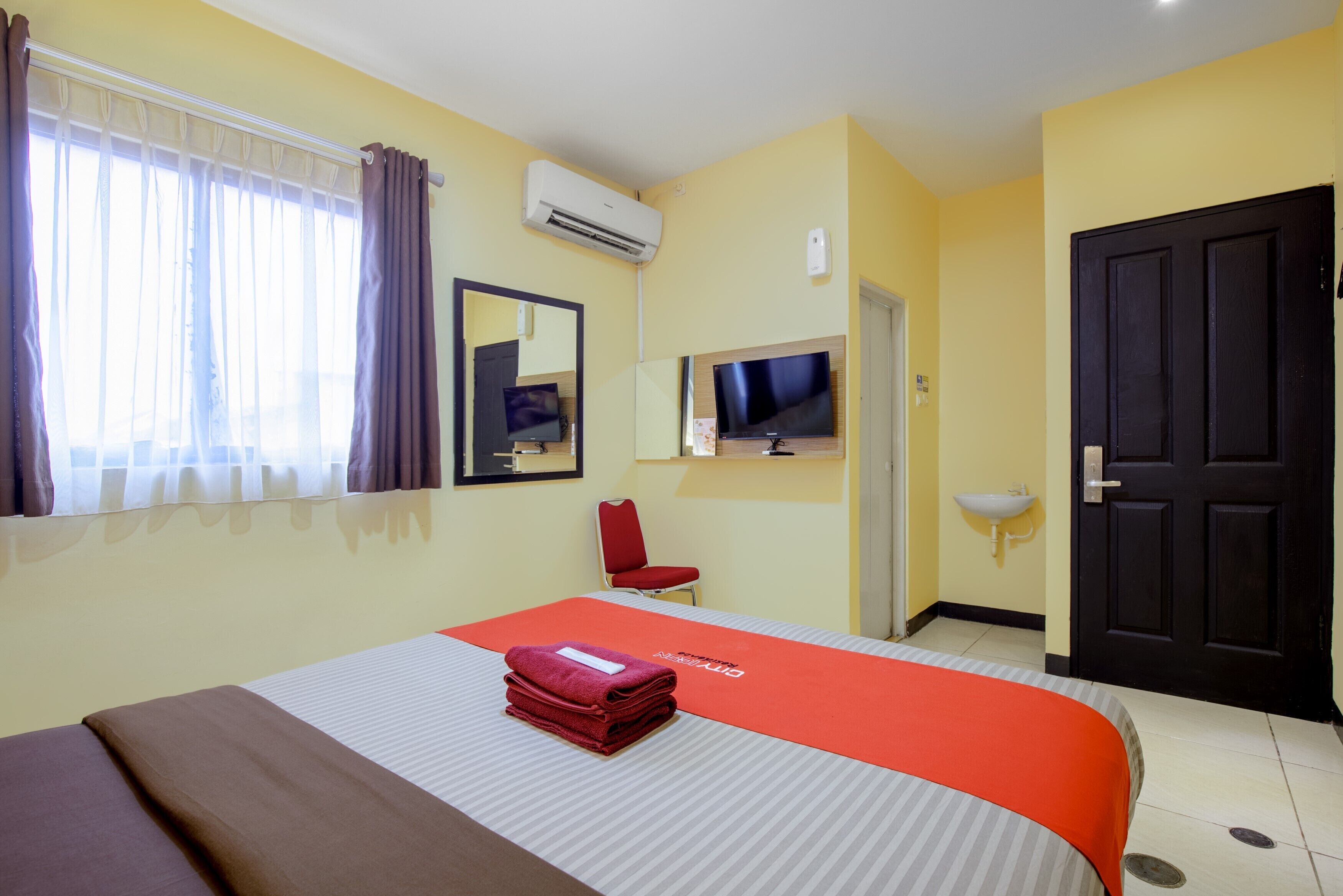 Une chambre d’hôtel avec un lit, une télévision, une chaise et une porte.