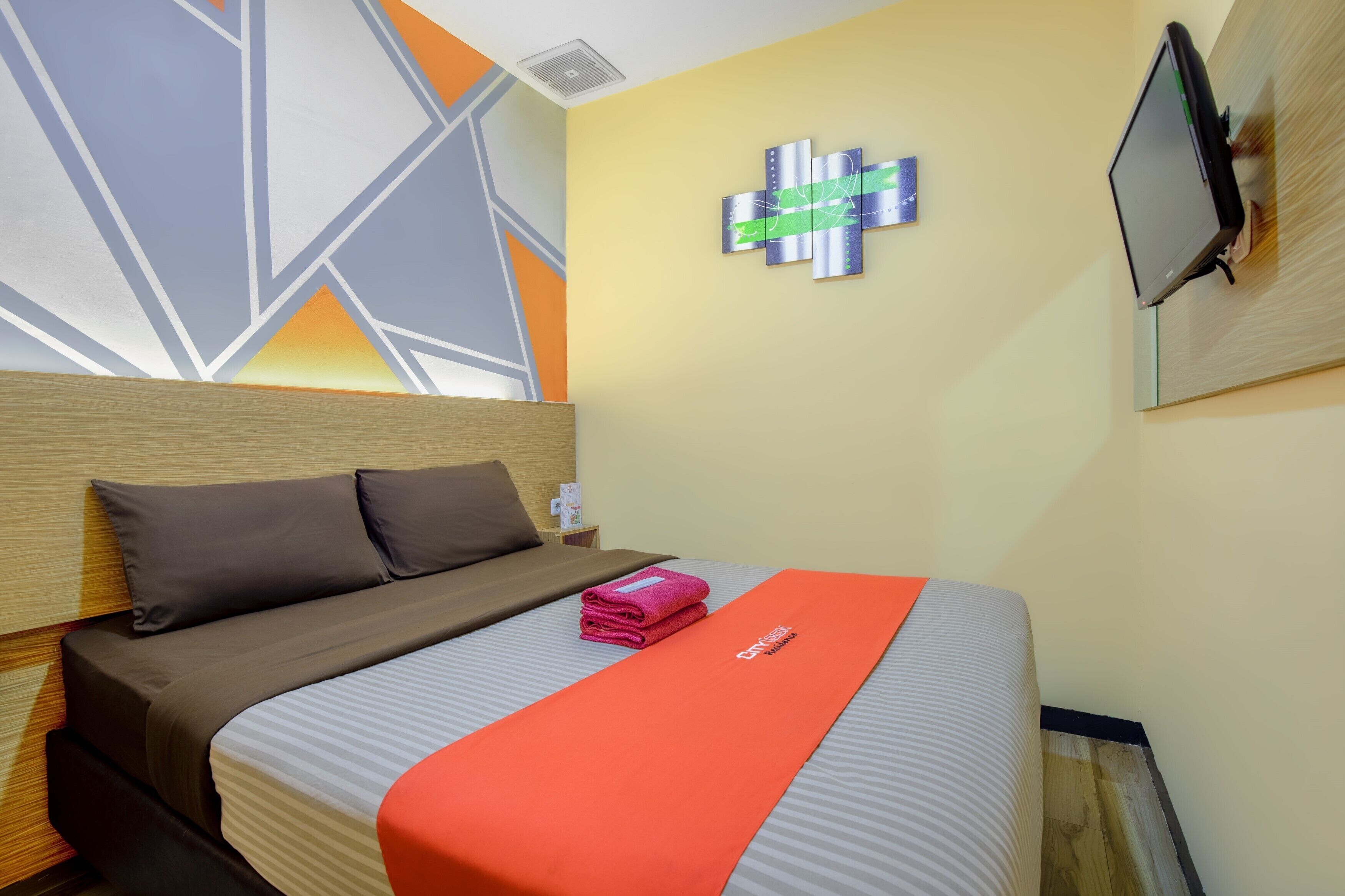 A hotel room with a bed, a TV, a wall art piece, and a folded towel on the bed.