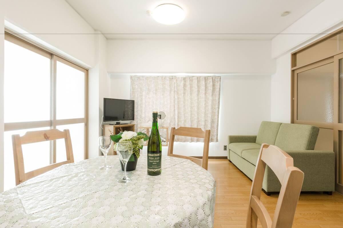 A living room with a round table, two chairs, a sofa, a television, and a window with curtains.