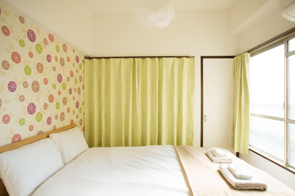A hotel room with a bed, a window with curtains, and a wall with a floral pattern.