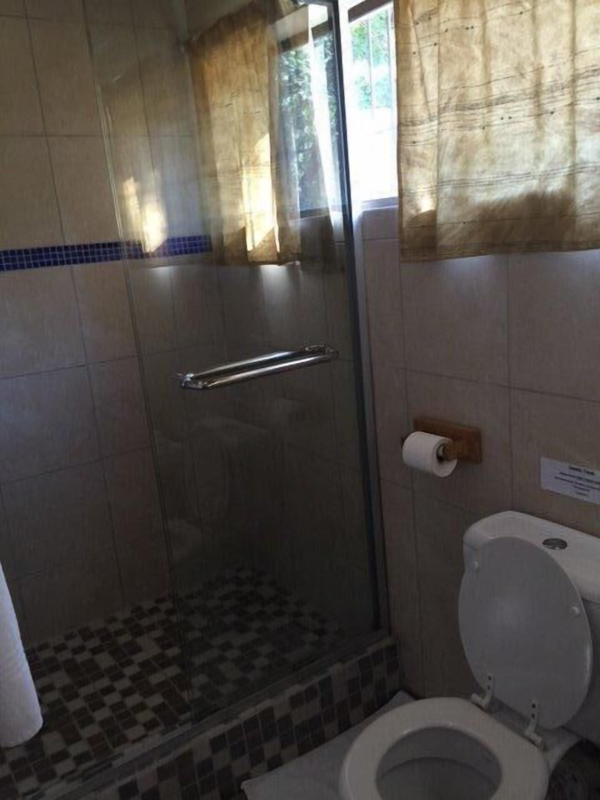 A bathroom with a glass shower enclosure, a toilet, and a tiled floor.