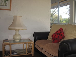 A living room with a glass-top side table, a lamp, a sofa with a patterned cushion, and a window with a view of trees. - Pinetown Lala Land (Kloof)