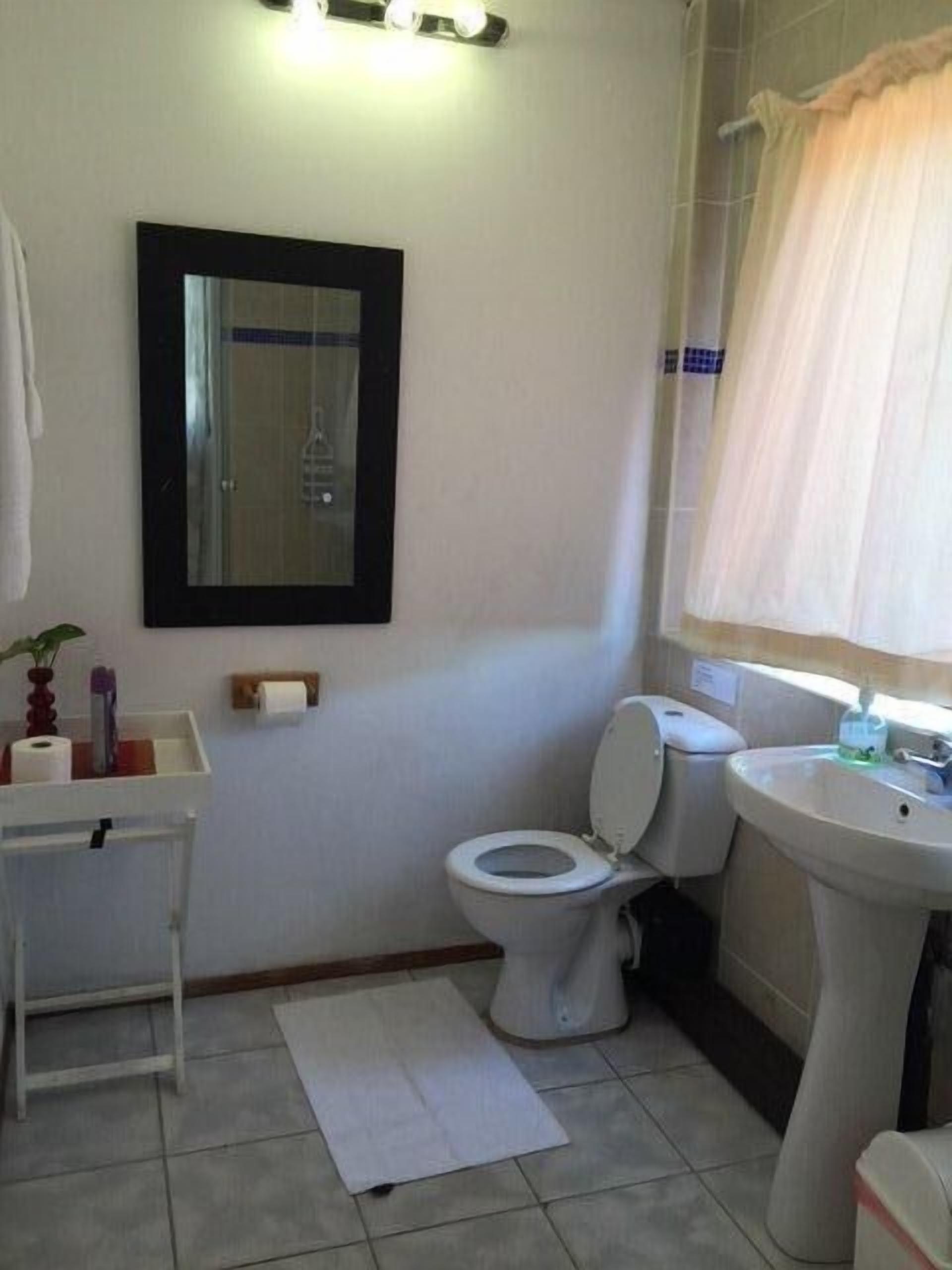 Une salle de bain équipée de toilettes, d’un lavabo, d’un miroir et d’une petite table sur laquelle sont posés des articles de toilette.