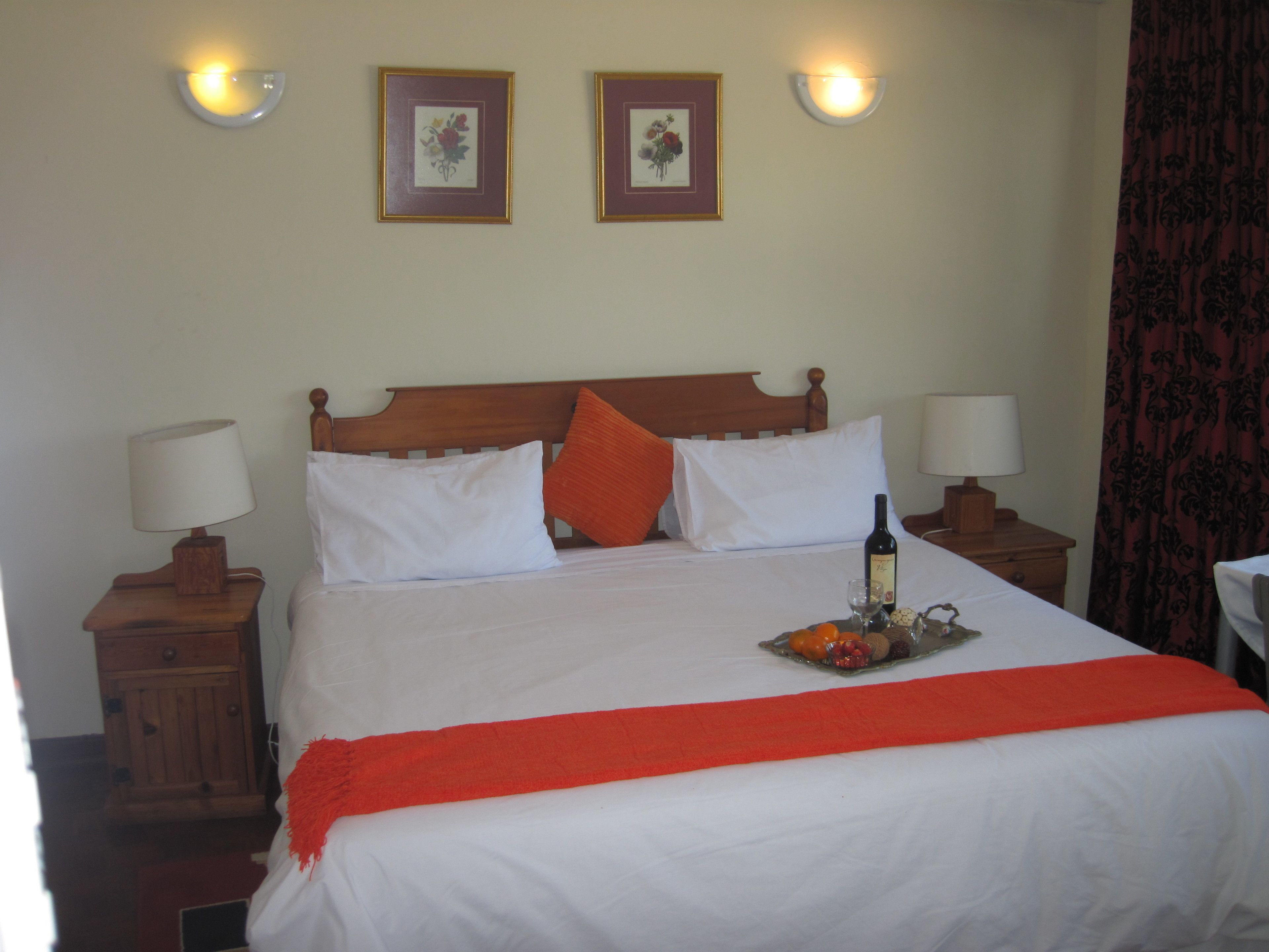 A neatly made bed with white linens, a red throw blanket, and a bottle of wine on the nightstand.