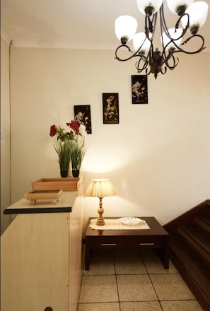 A small, well-lit room with a wooden desk, a lamp, and a potted plant. There are three framed pictures on the wall and a staircase to the right. - Pinetown Lala Land (Kloof)