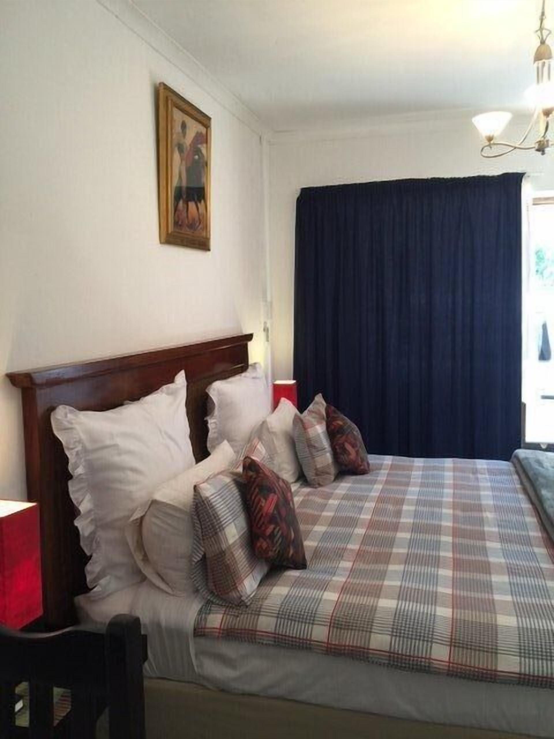 A bedroom with a wooden headboard, a plaid bedspread, and a dark curtain.
