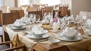 A dining table set with white plates, bowls, and wine glasses, with salt and pepper shakers and a small vase of flowers.