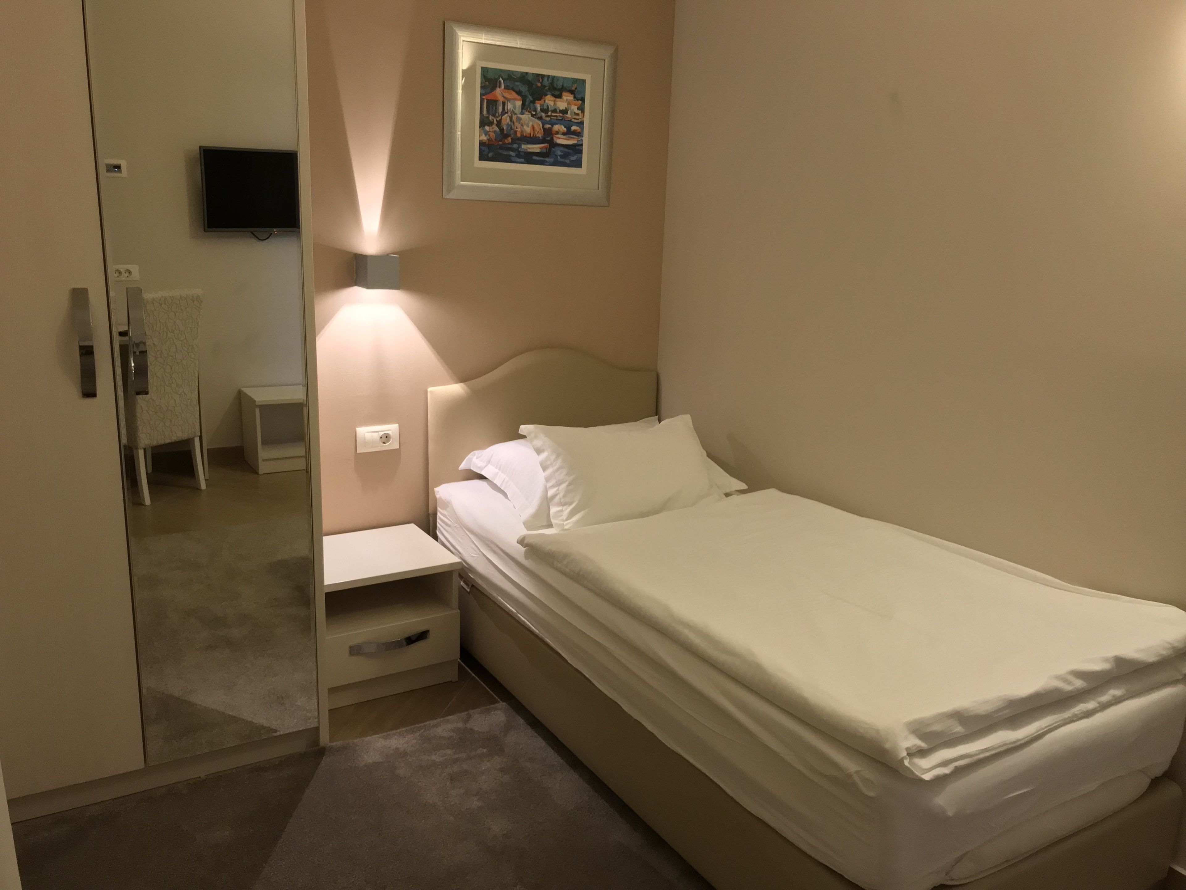 A hotel room with a bed, bedside table, lamp, and a painting on the wall.