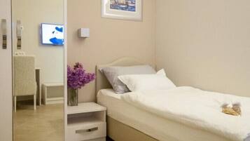 A small, modern bedroom with a bed, a nightstand, a mirror, a framed picture on the wall, and a TV on the wall.