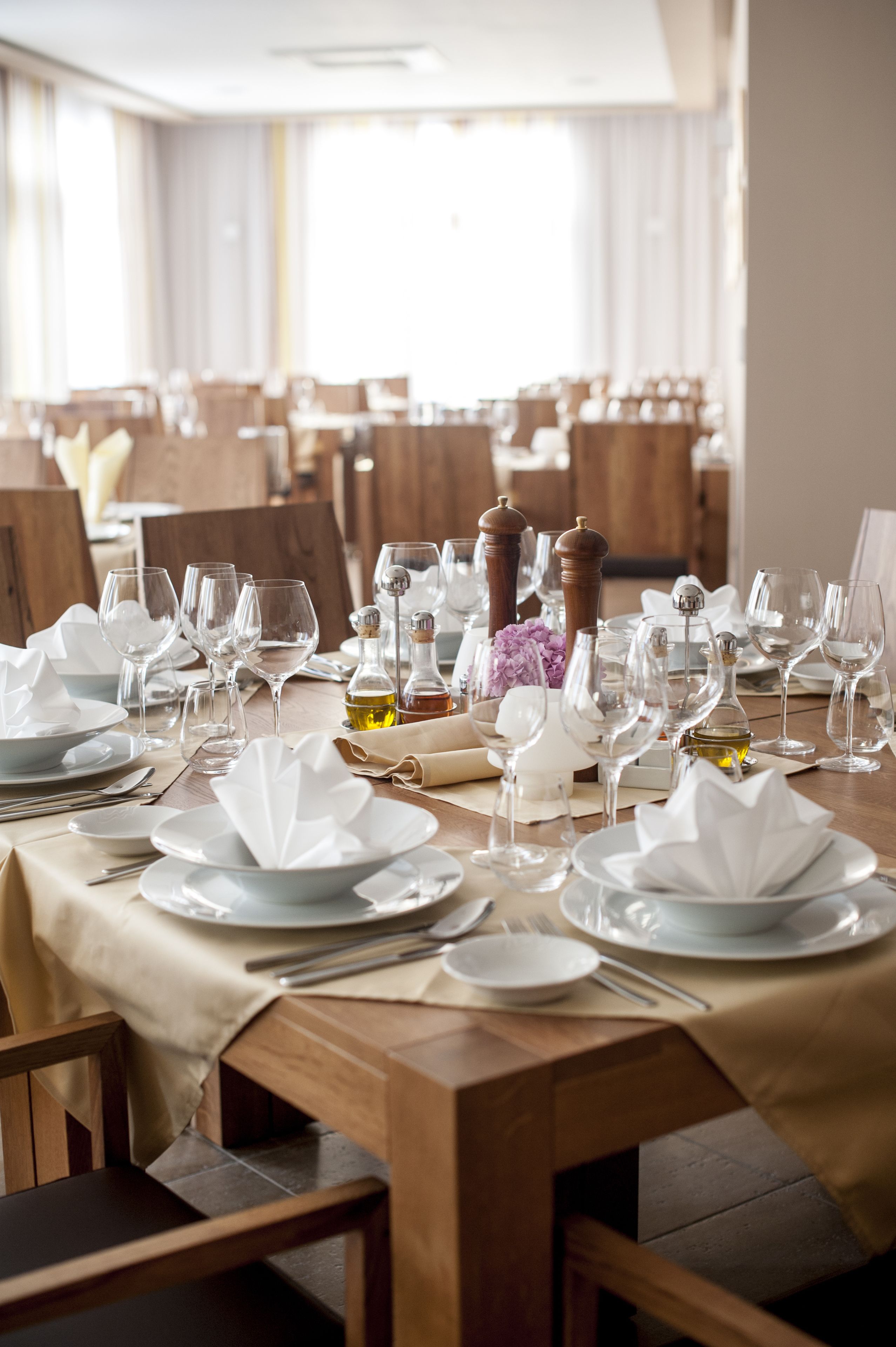Un espace repas avec des tables dressées pour le service, agrémenté de nappes blanches, d’assiettes, de verres et de couverts.