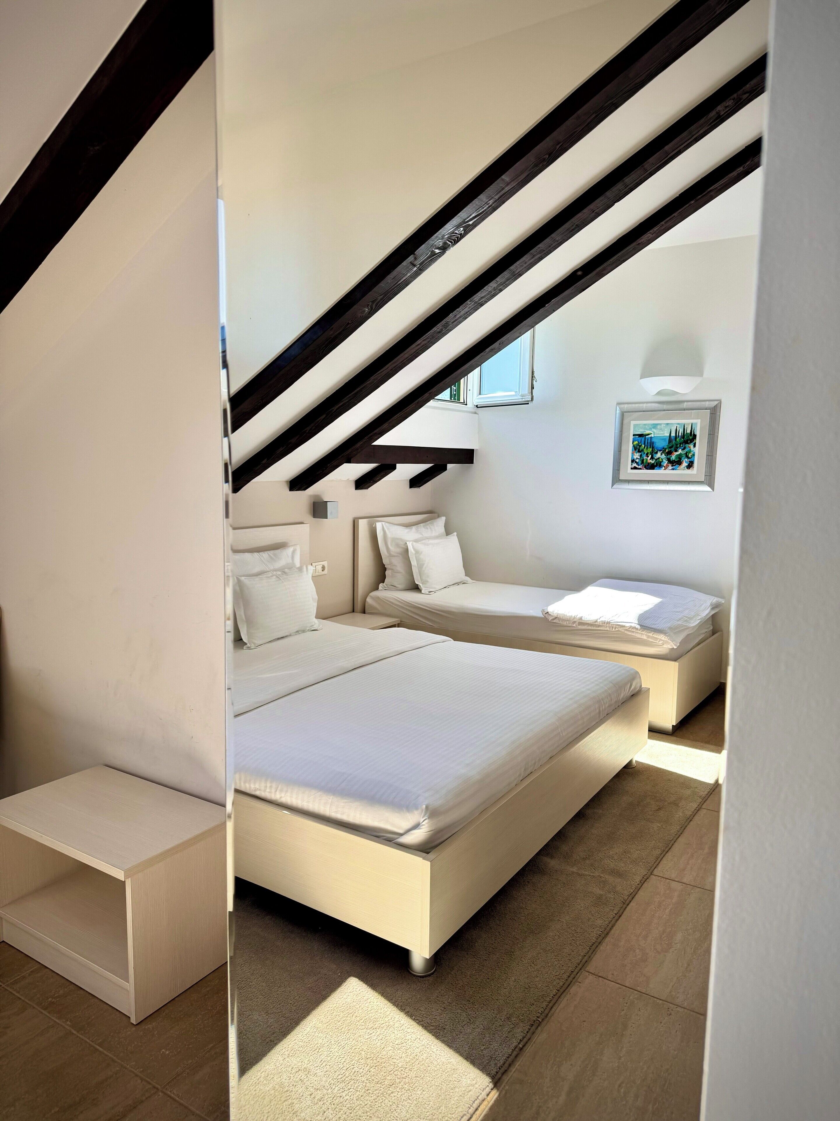 Ein modernes Schlafzimmer mit zwei Betten, einem Oberlicht und einem gerahmten Bild an der Wand.