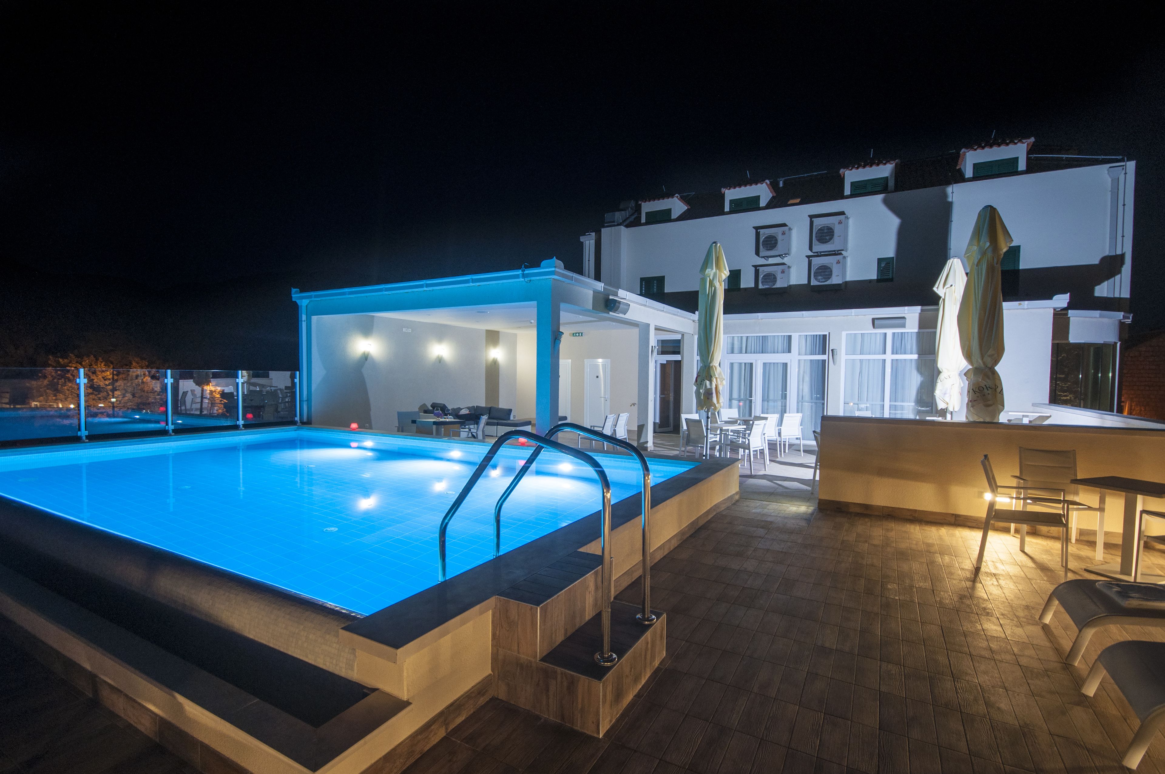 An indoor swimming pool with a covered area, a bar, and a seating area with chairs and tables.