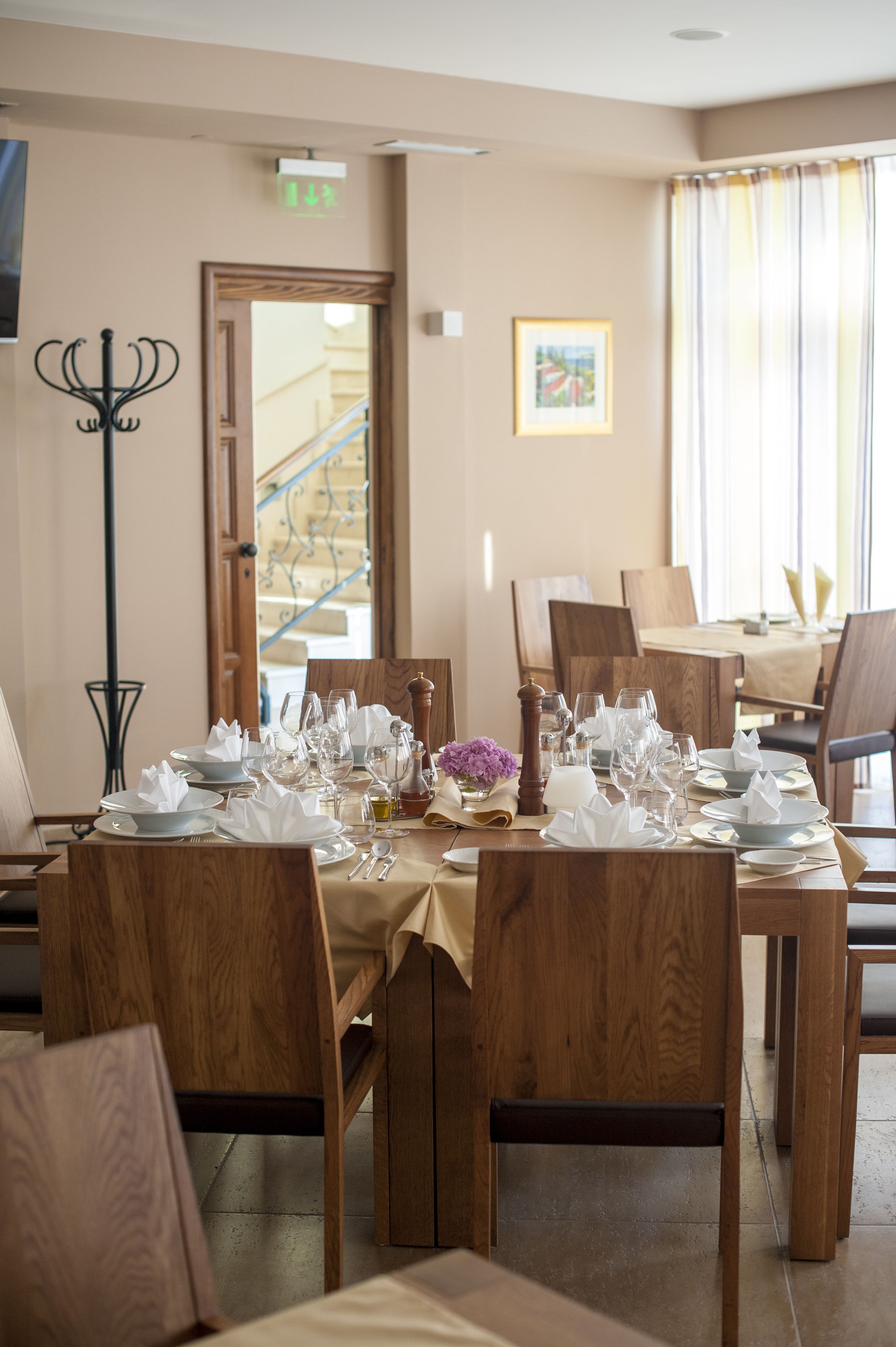 A dining area with wooden tables and chairs, a chandelier, and a staircase in the background.