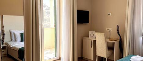 Habitación de hotel con cama, escritorio, silla, televisor y puerta corrediza de vidrio al exterior.