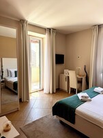 Habitación de hotel con cama, escritorio, silla, televisor y puerta corrediza de vidrio al exterior.