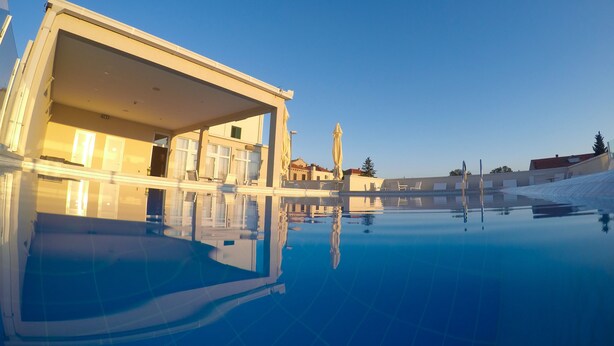 A modern hotel with a pool, a covered outdoor area, and a clear blue sky.